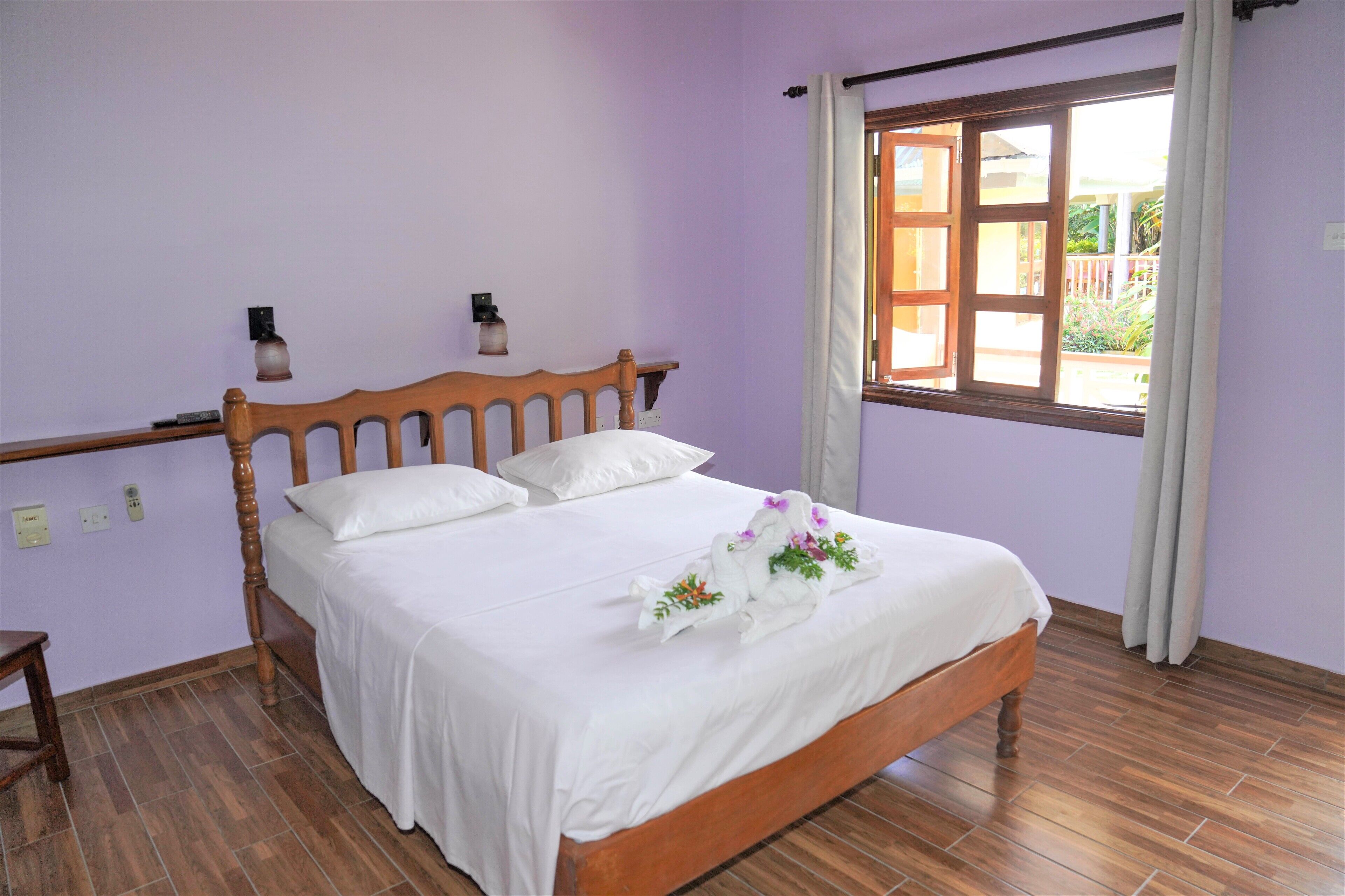 Un dormitorio con cama de madera, ropa de cama blanca, una mesita de noche y una ventana con cortinas.
