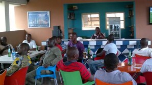 A group of people seated at tables in a room with a television mounted on the wall. - Esado Suites and Conference Oregun (Lagos)