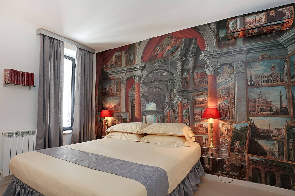 Ein Schlafzimmer mit einem großen Bett, einem Fenster mit Vorhängen, einem Heizkörper und einer Wand mit einem Stadtbild-Wandgemälde.