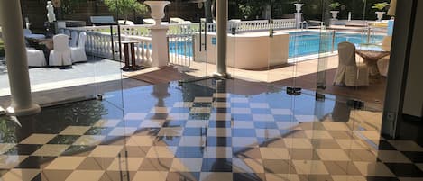 Zona de piscina con suelo a cuadros, sillas blancas y sombrillas.