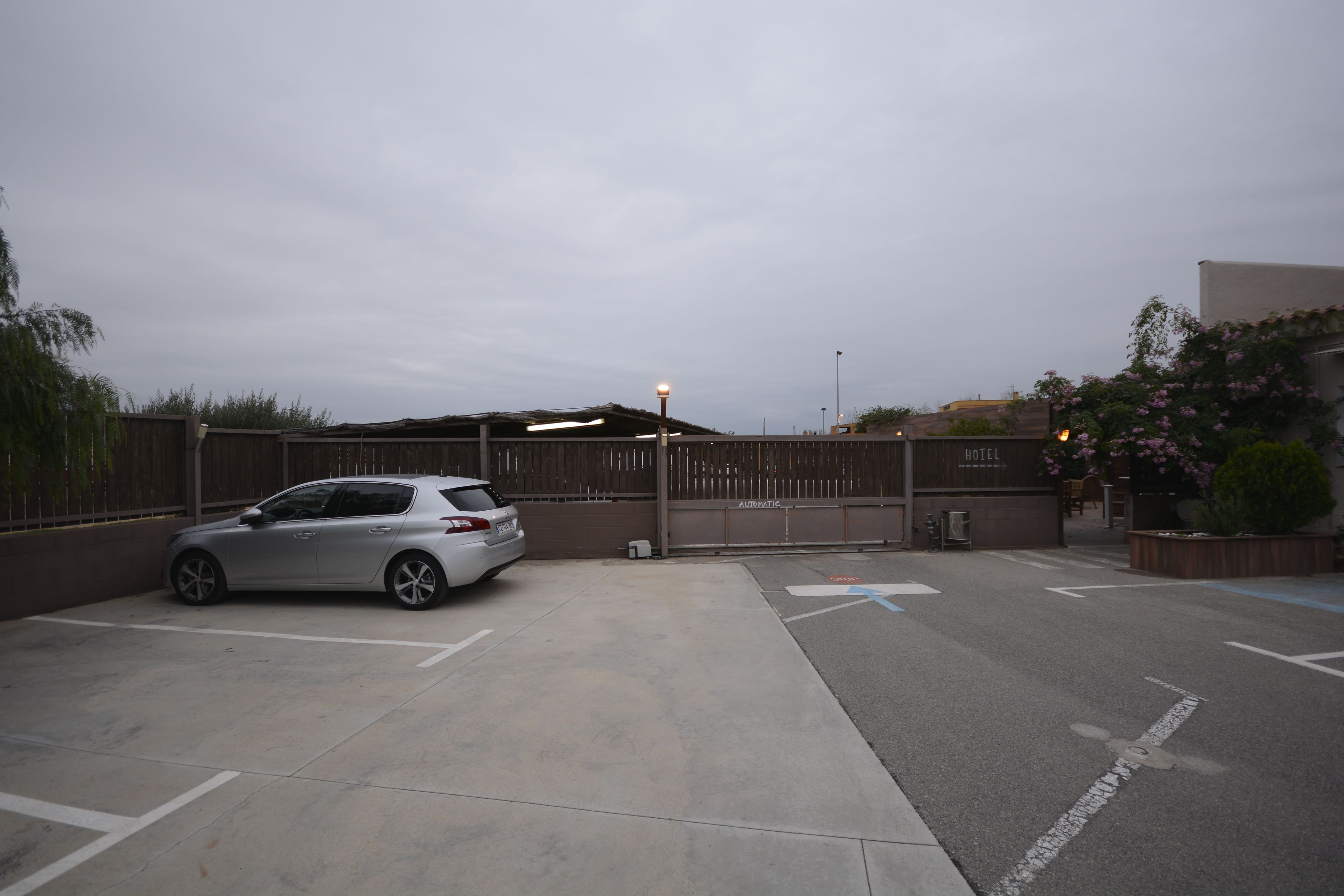 A parking area with a car, a gated entrance, and a building labeled "HOTEL" in the background.