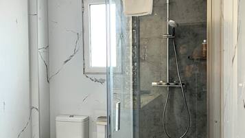A modern bathroom with a glass-enclosed shower, a toilet, and a marble wall.