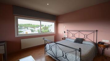 A bedroom with a large window, a bed with a metal frame, a bedside table, and a nightstand.