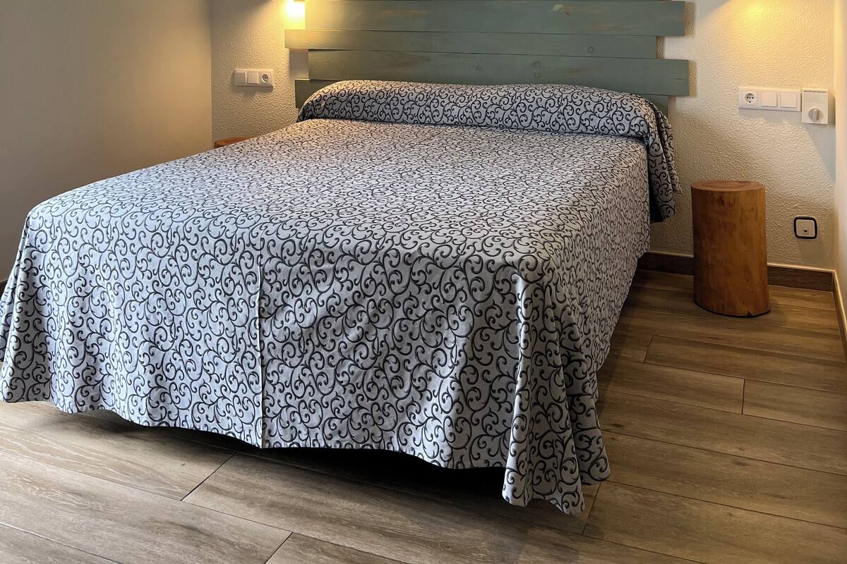 A bedroom with a bed, a ceiling fan, a nightstand, and a wall-mounted light.