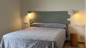 Quarto com cama, ventilador de teto, mesa de cabeceira e luminária na parede.