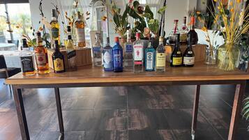 Une table de bar en bois, sur laquelle sont disposées de manière ordonnée différentes bouteilles d’alcool, notamment du whisky, de la vodka et du gin.