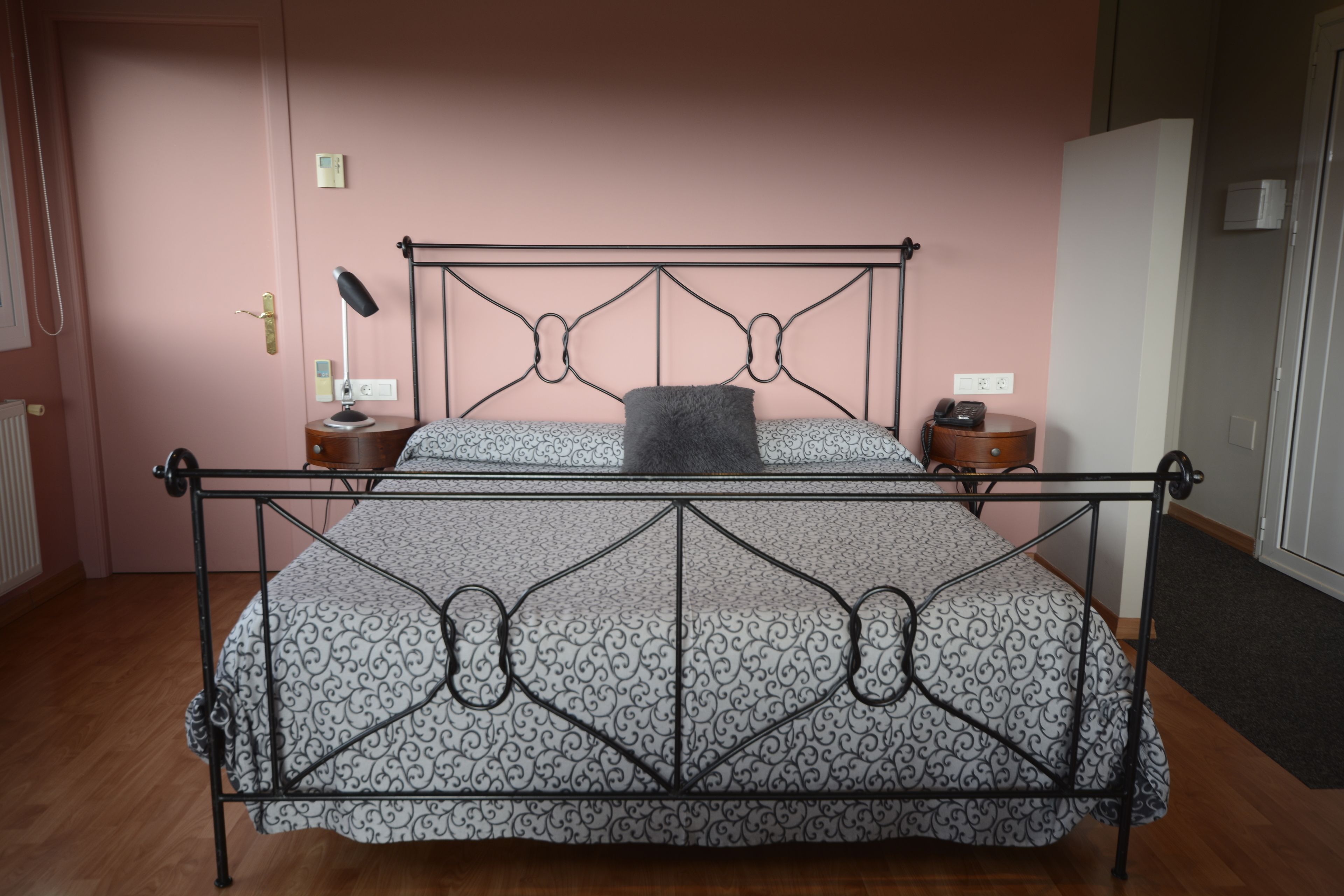 Una cama con estructura metálica y ropa de cama estampada, una lámpara de noche, una mesita de noche y un teléfono.