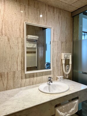 A bathroom with a marble wall, a sink, a mirror, a towel rack, and a handheld showerhead.