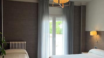 A hotel room with two beds, a radiator, a table, a lamp, and a view of the outdoors through a glass door.