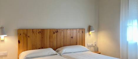 Una cama doble con cabecera de madera, dos mesitas de noche y un ventilador de techo en una habitación con suelo de madera y paredes blancas.