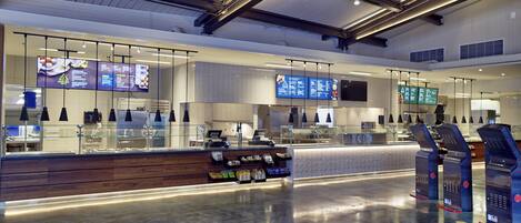 Un espace de restauration moderne et bien éclairé, situé dans l’aéroport, avec de nombreux coins salon et des écrans numériques affichant les menus.
