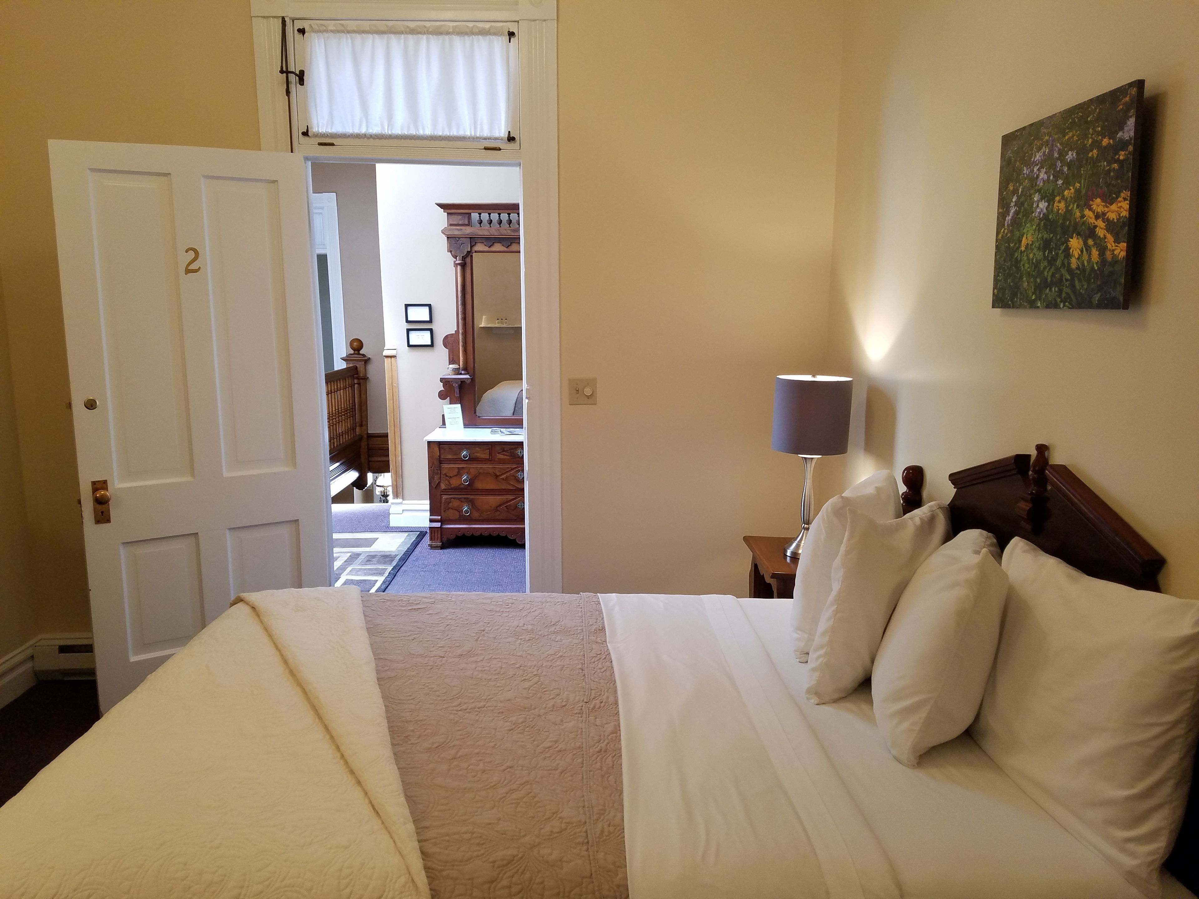 Une chambre à coucher avec un lit, une table de chevet, une lampe, une commode et un tableau au mur.