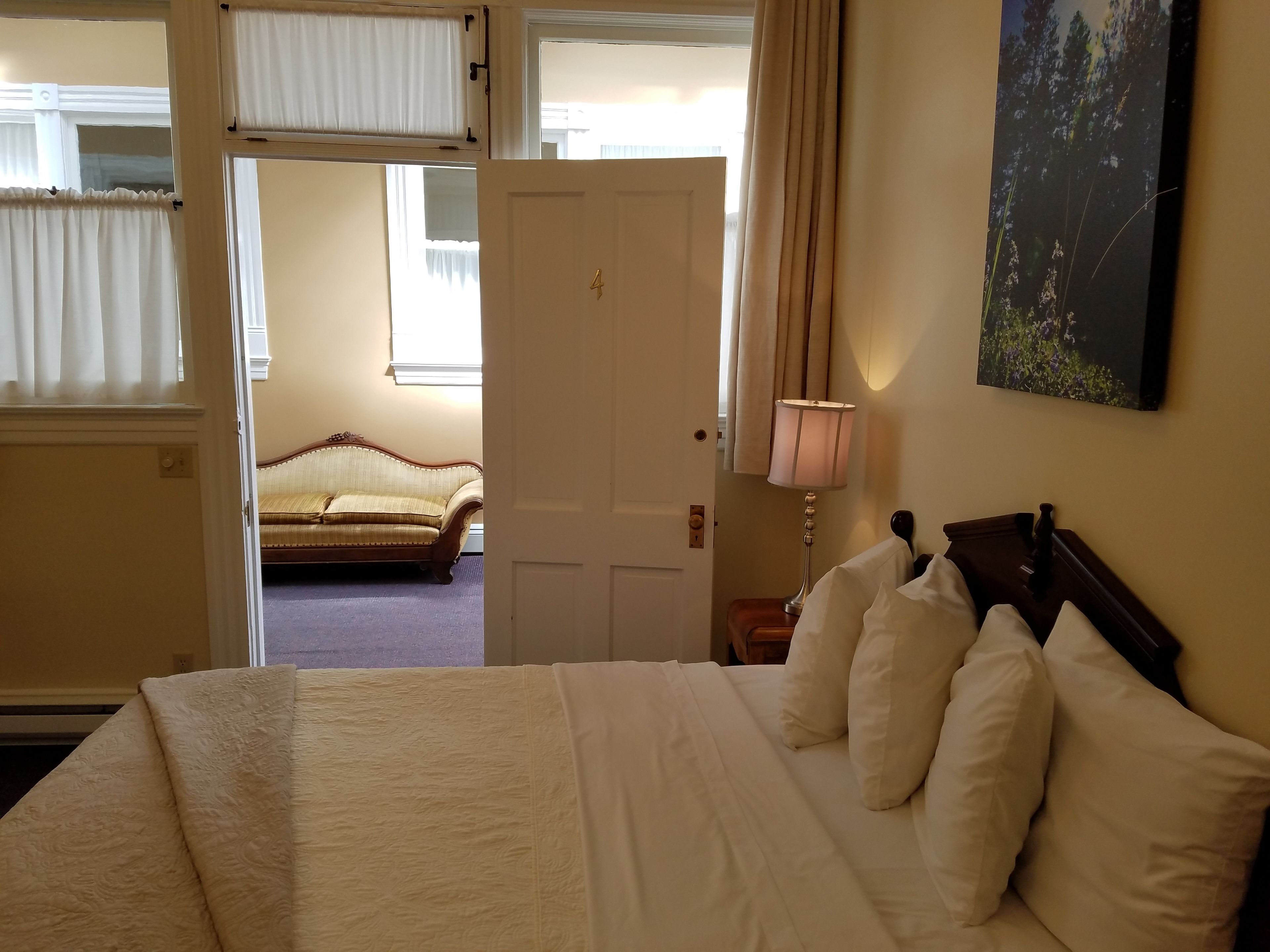 A hotel room with a bed, a nightstand, a lamp, a sofa, and a painting on the wall.