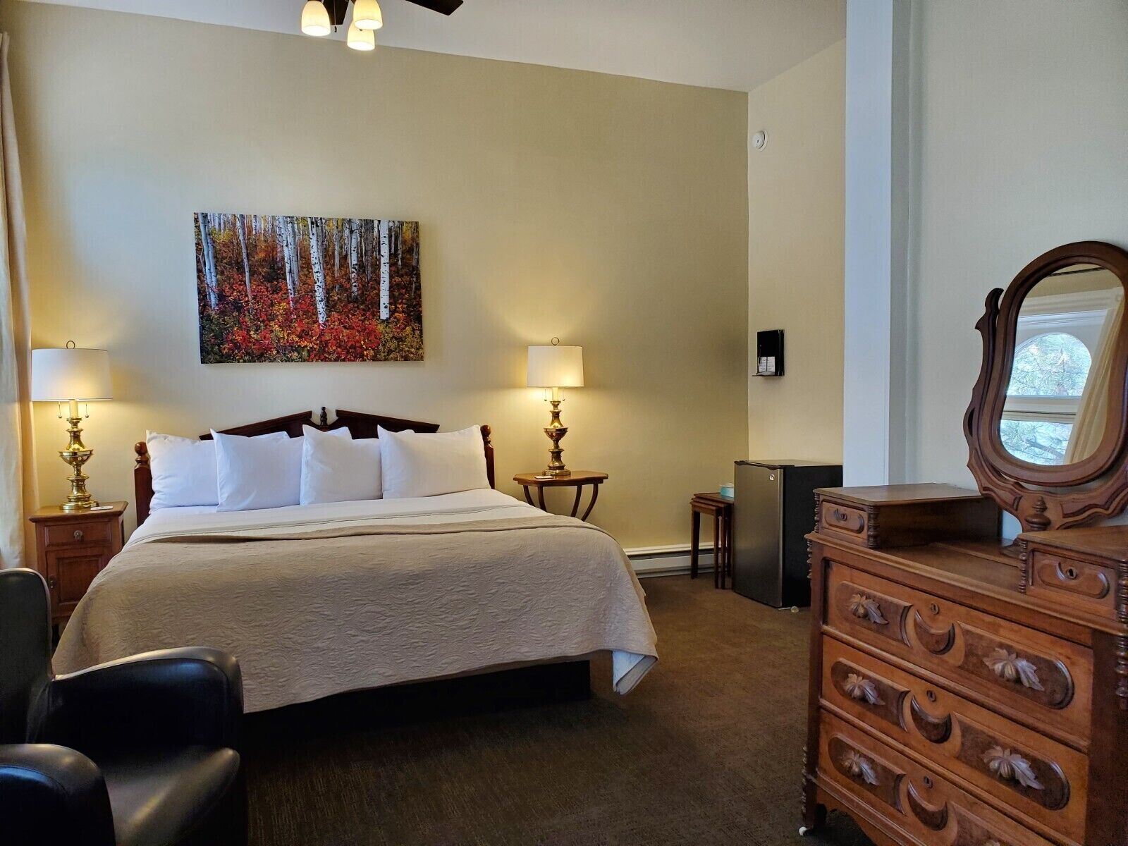 Una habitación de hotel con una cama grande, dos mesitas de noche con lámparas, un aparador, un espejo y un cuadro en la pared.