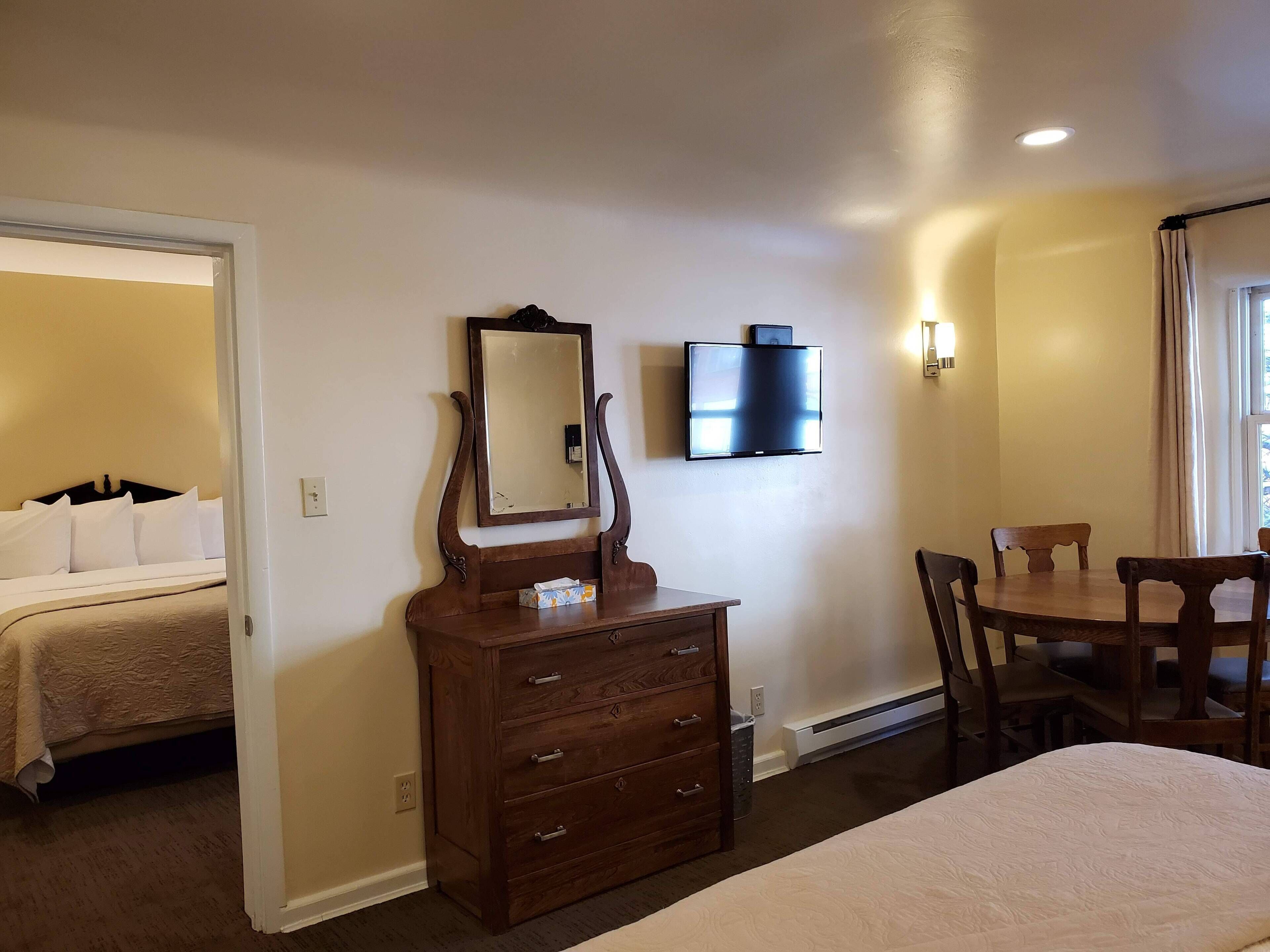 Una habitación de hotel con cama, cómoda, televisión montada en la pared y una mesa de comedor con sillas.