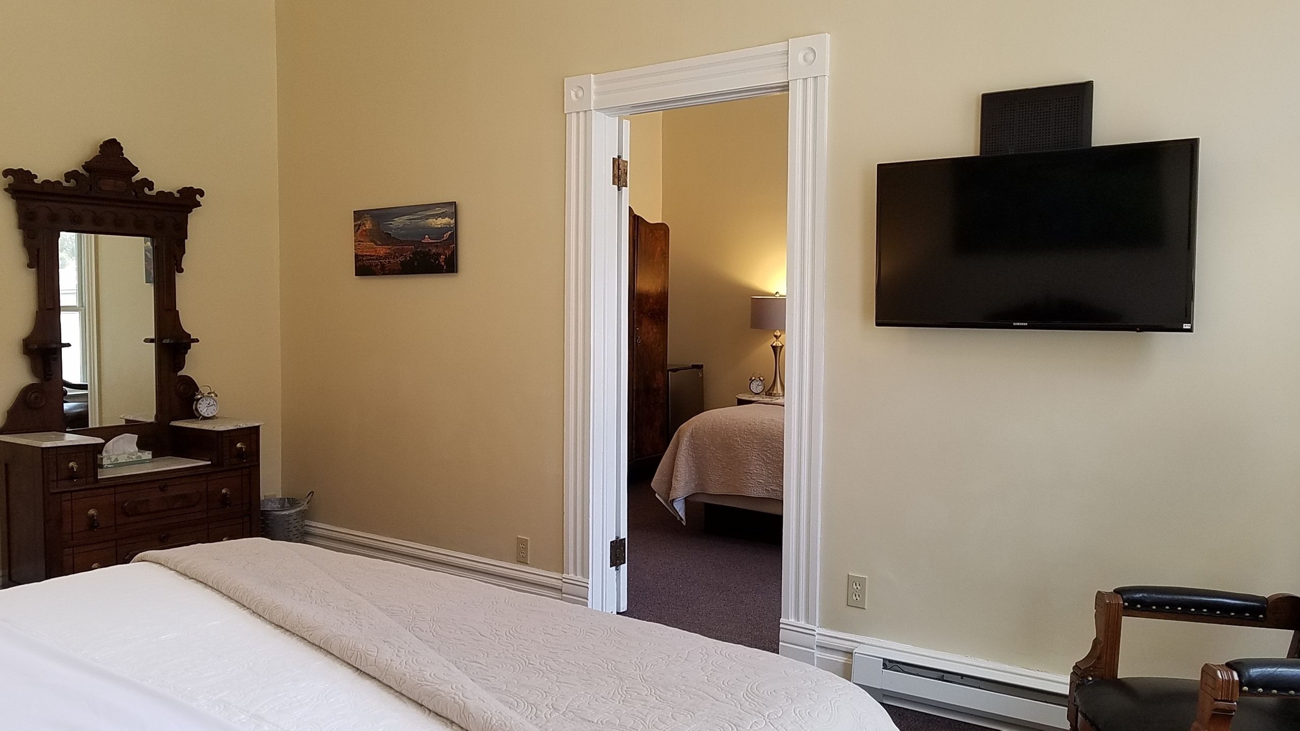 A hotel room with a bed, a television mounted on the wall, a mirror, and a painting on the wall.
