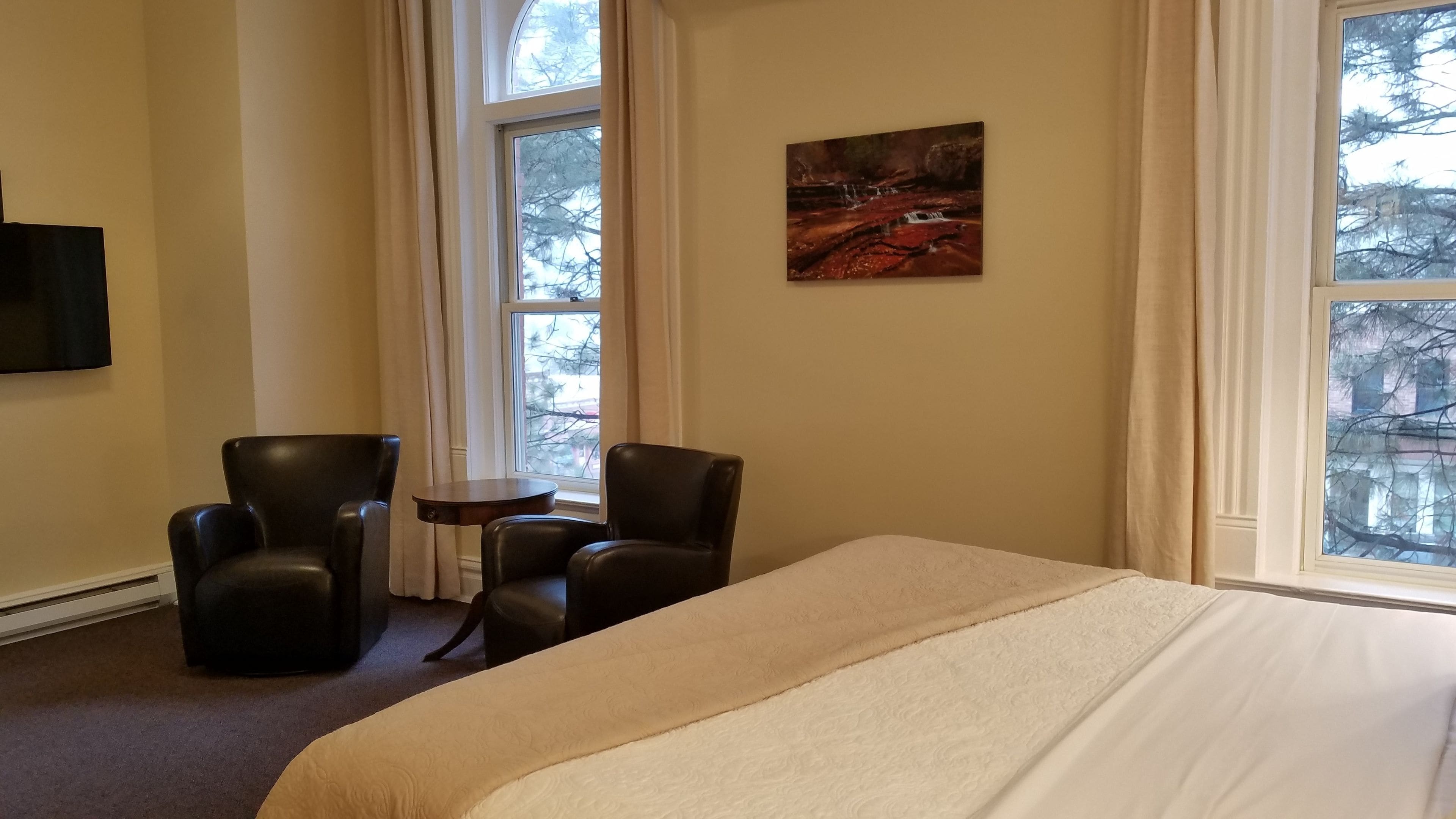 A hotel room with a large bed, two armchairs, a small table, and a painting on the wall.