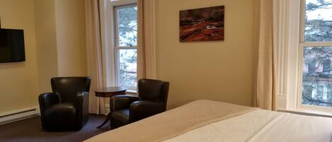 A hotel room with a large bed, two armchairs, a small table, and a painting on the wall.