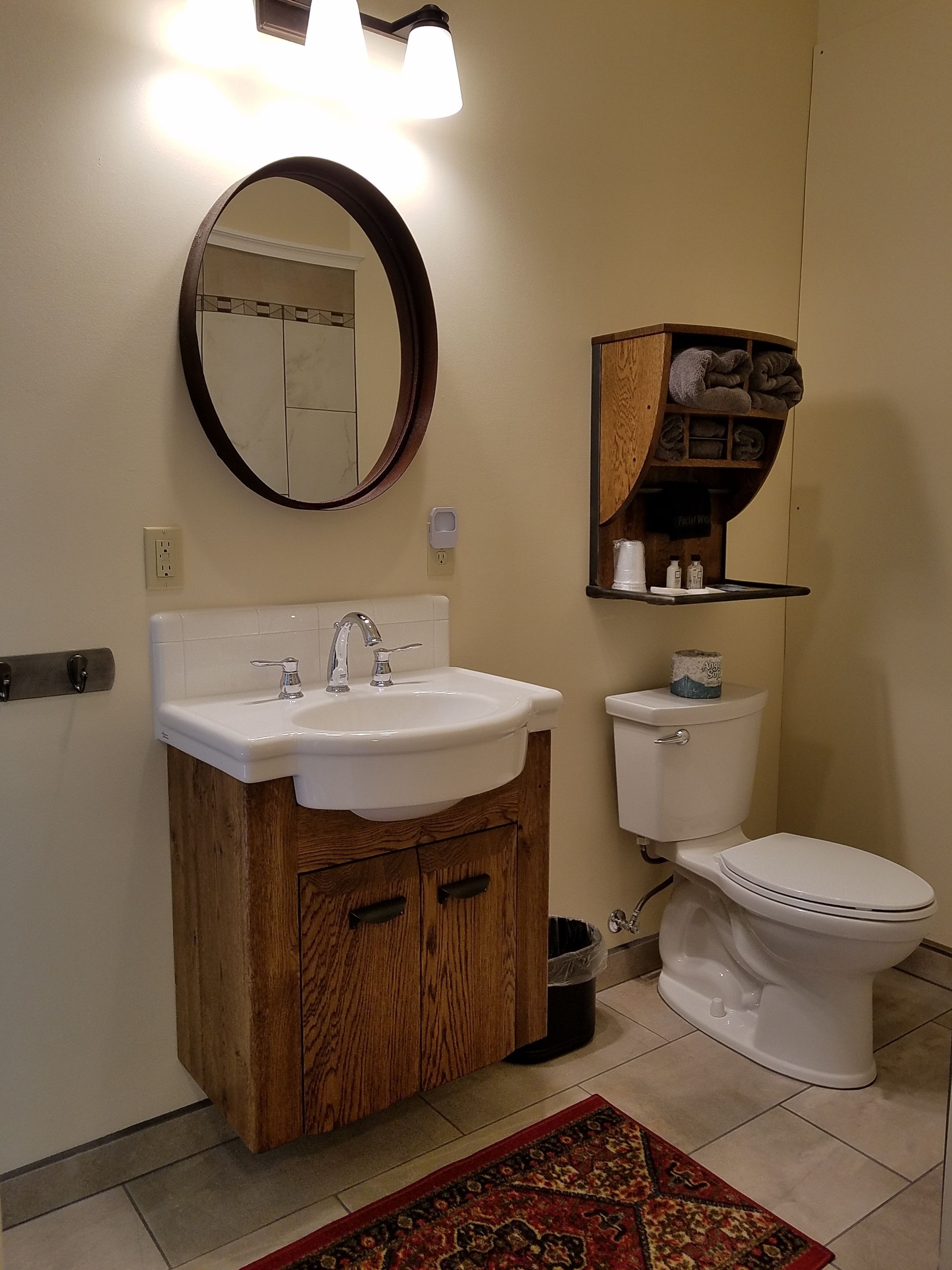 Een badkamer met een witte wastafel, een houten opbergmeubel, een ronde spiegel, een toilet en een plank met handdoeken.