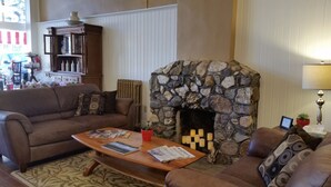 Un salón acogedor con chimenea de piedra, un sofá marrón, una mesa de centro con revistas y una maceta roja sobre la mesita.