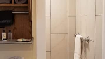 Un bany amb vàter, penjador de tovalloles, dutxa i prestatge amb tovalloles i productes de tocador.