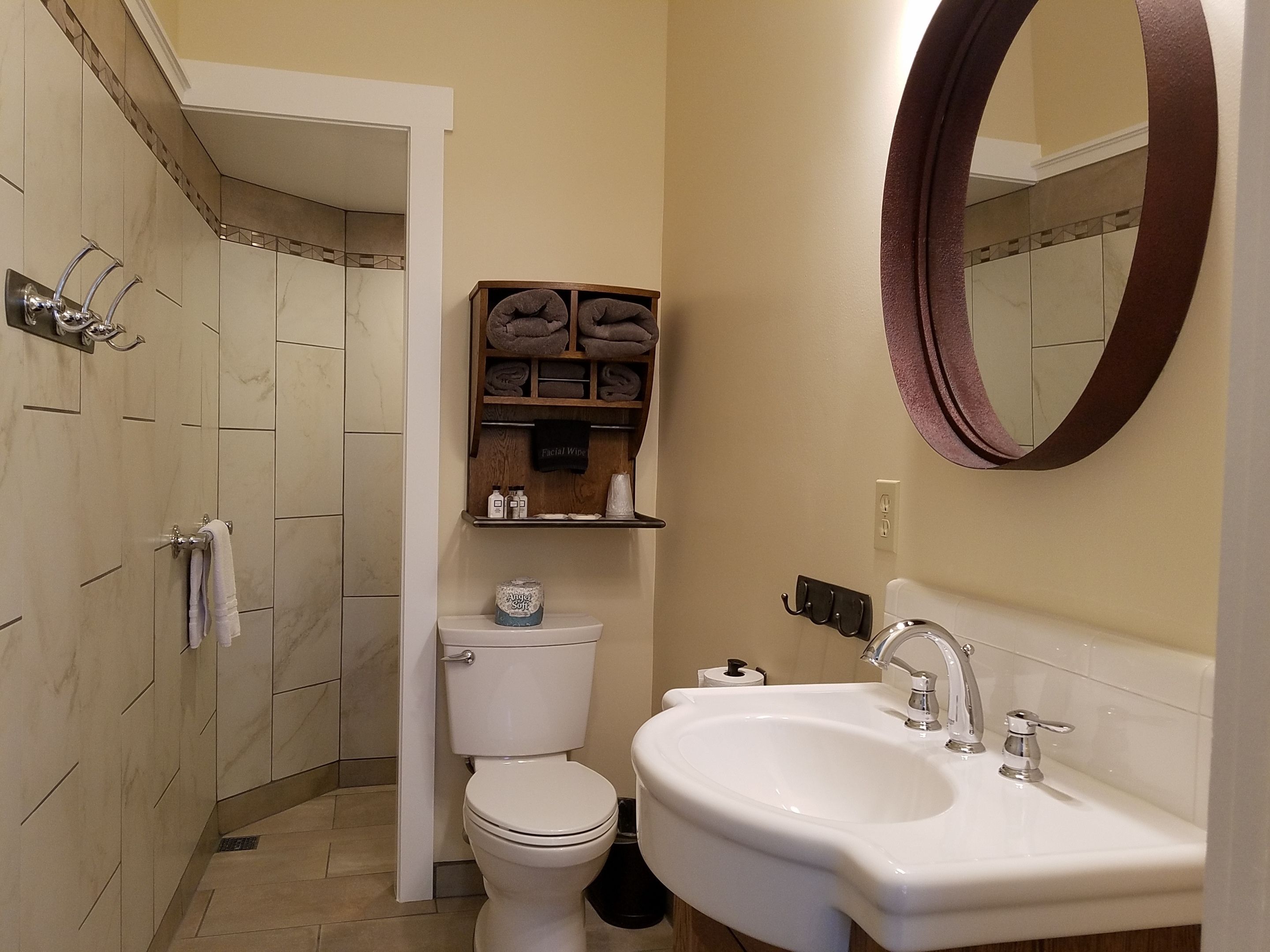 Un baño con inodoro, lavabo y espejo. Hay toallas y artículos de aseo en un estante.