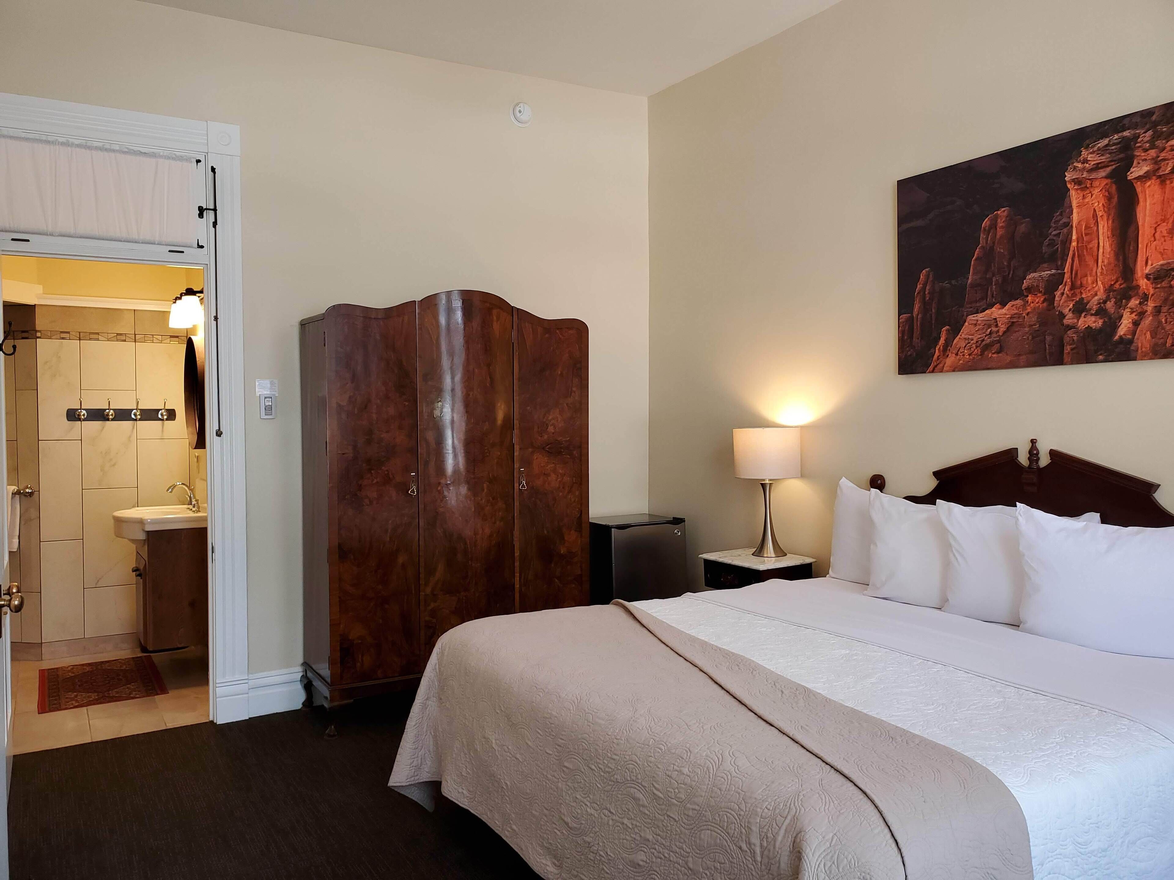 Una habitación de hotel con cama, armario, baño y un cuadro en la pared.