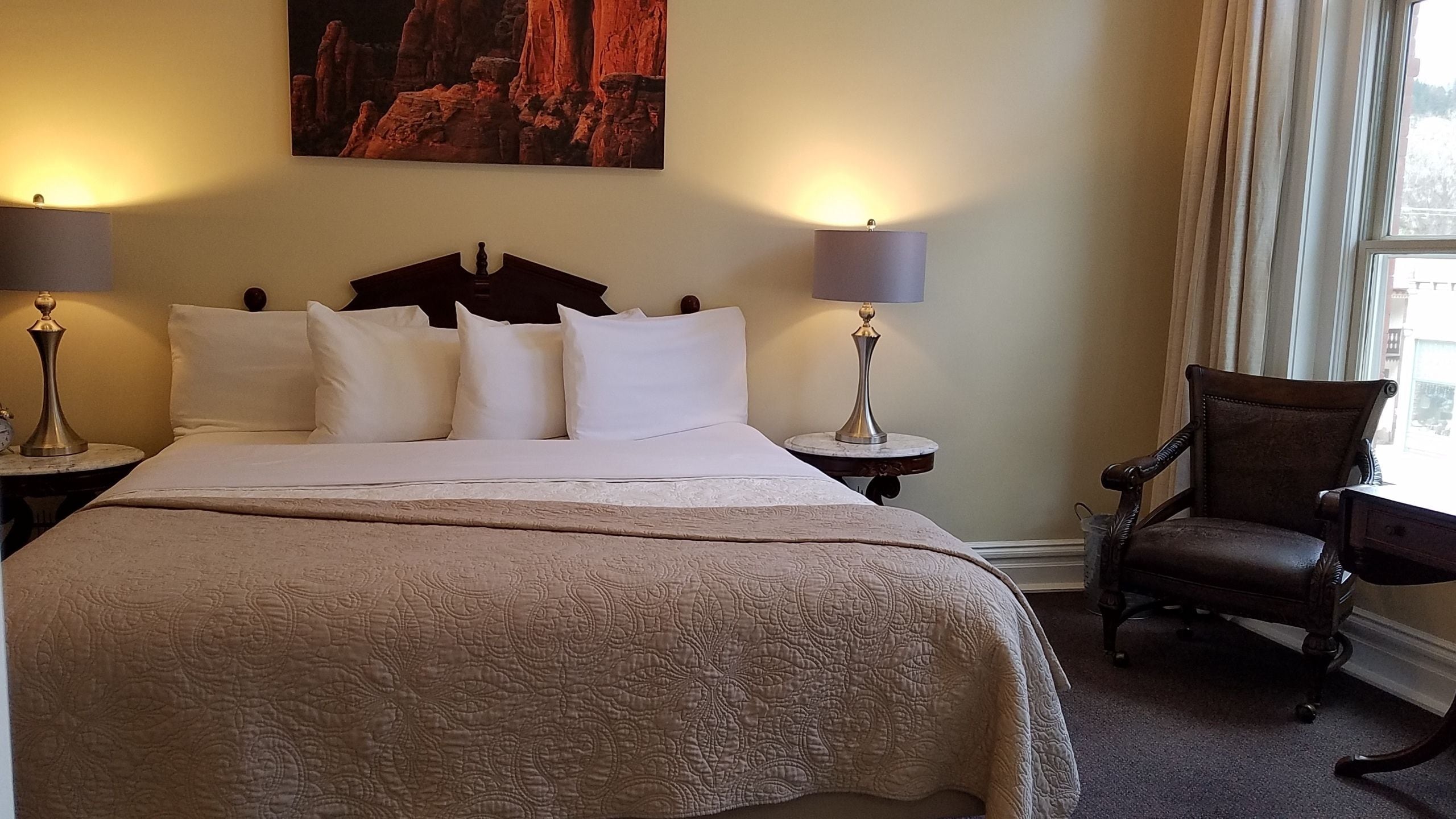 A hotel room with a large bed, two bedside lamps, a chair, and a painting on the wall.