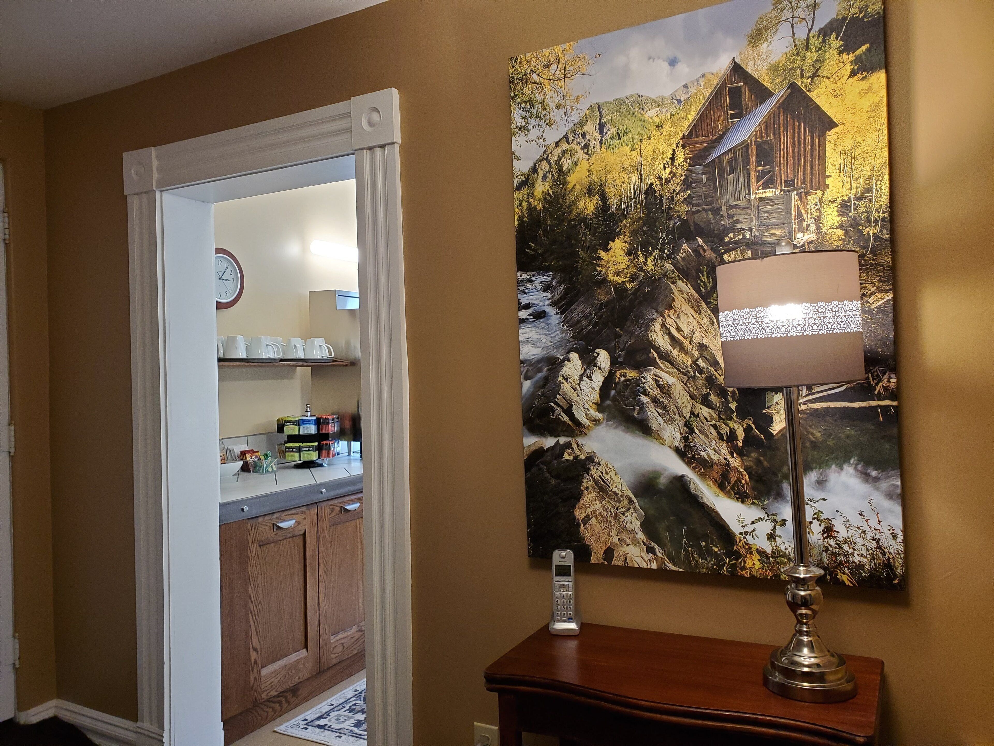 A hallway with a wooden cabinet, a clock, and a painting of a cabin by a stream.