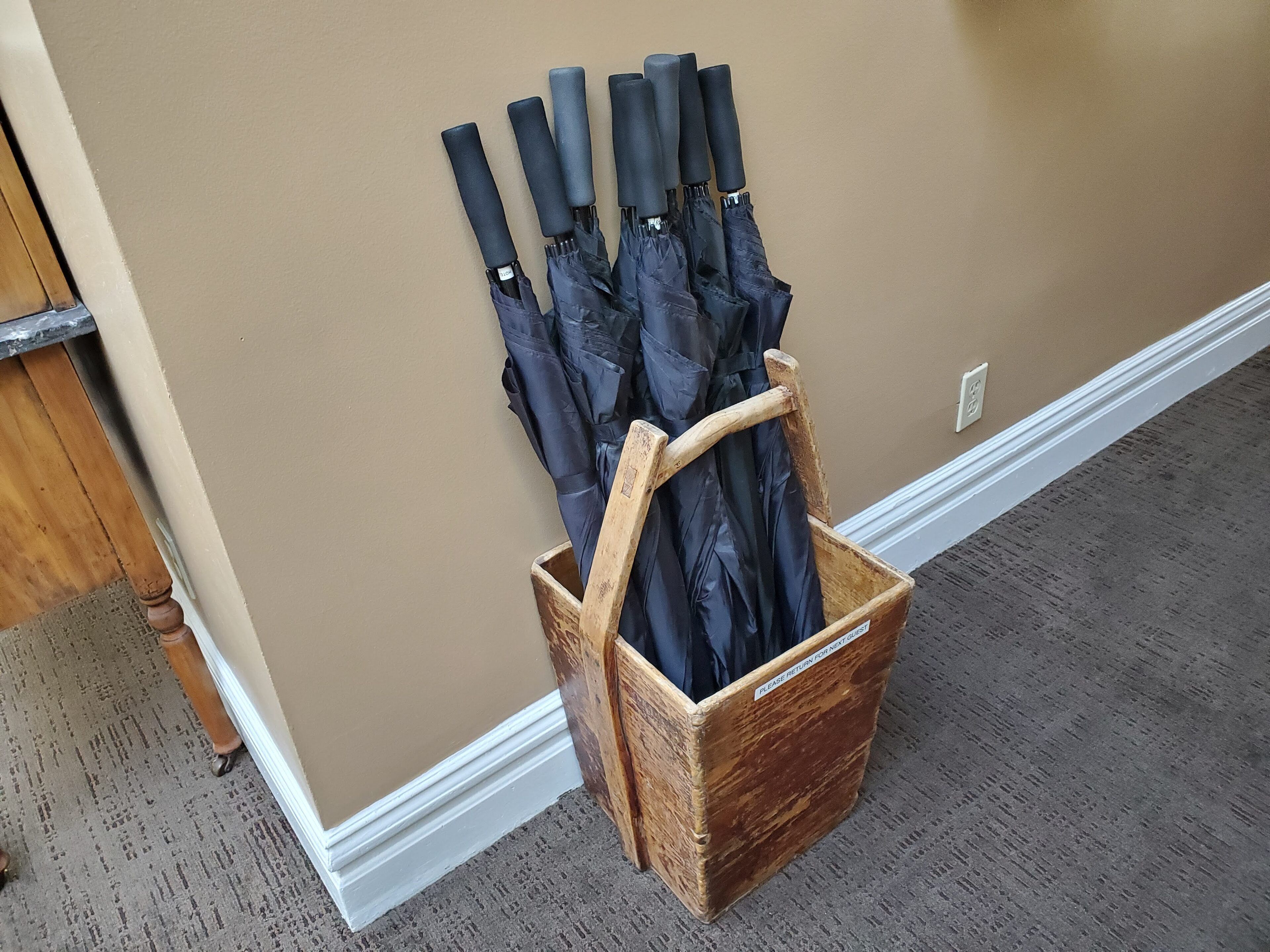 A wooden basket holding several umbrellas against a beige wall.