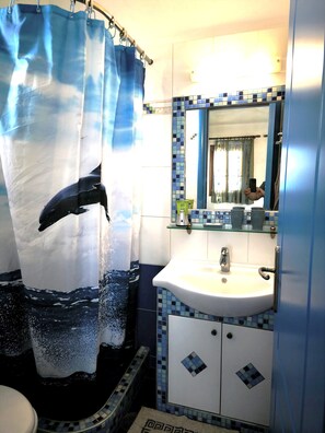 A bathroom with a shower curtain depicting a whale, a sink with a mirror above it, and tiled walls. - Ammoudia Studios (Naxos)