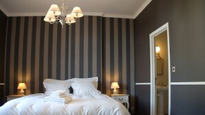A bedroom with a large bed, two bedside tables with lamps, a chandelier, and a door leading to a bathroom. - Hotel Vorsen (Gingelom)