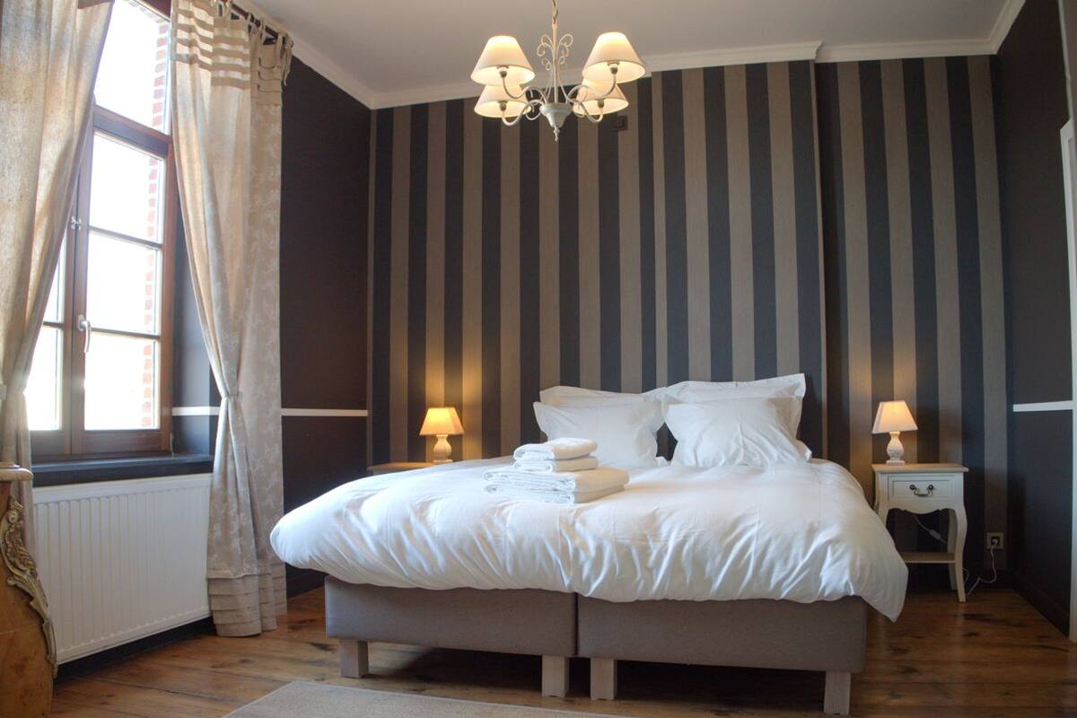 Une chambre à coucher avec un lit, des lampes de chevet, un radiateur et une fenêtre avec des rideaux.