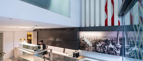Un espacio de oficina moderno con un escritorio de vidrio, una persona trabajando en una computadora y un gran mural urbano en la pared.