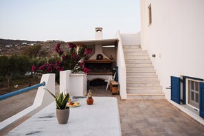 A terrace with a stone fireplace, a potted plant, and a table with a bottle and plate. - Joanna's Apartments (Naxos)