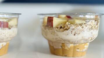 Dos vasos de vidrio transparentes con alimentos en capas, incluyendo frutas y granola, sobre una superficie blanca.
