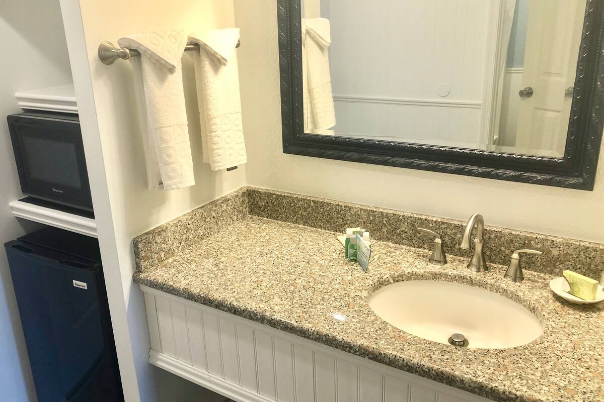 A bathroom with a granite countertop, a sink, a mirror, and towels hanging on a rack.