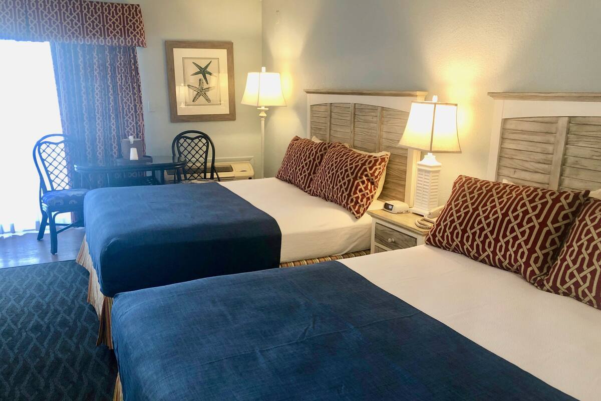A hotel room with two beds, a desk, chairs, and a fireplace.