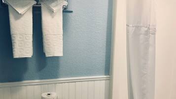 Un baño con inodoro, un cubo de basura, un estante con toallas dobladas y una bañera con cortina de ducha.