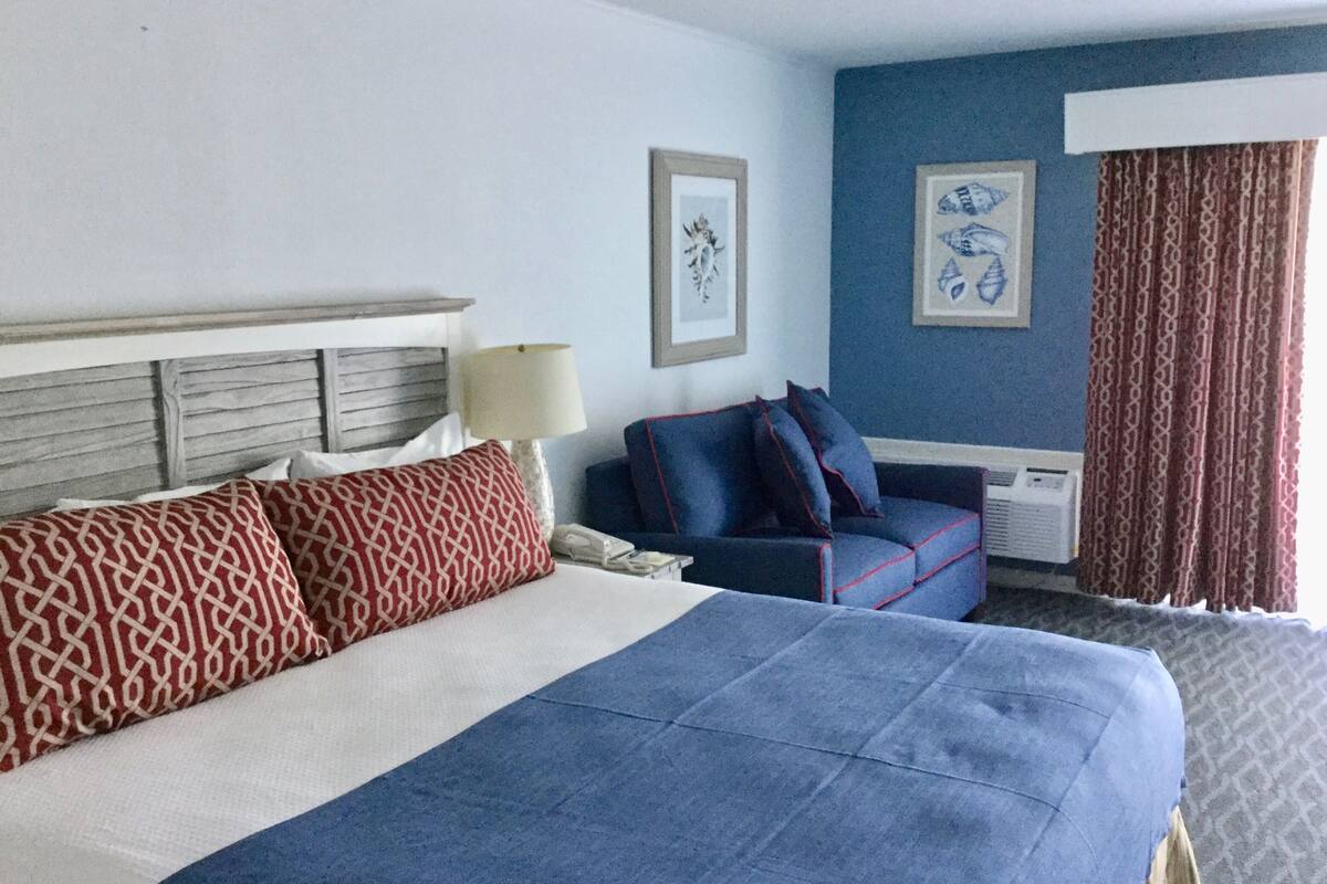 A hotel room with a large bed, a sofa, a desk, and a window with curtains.