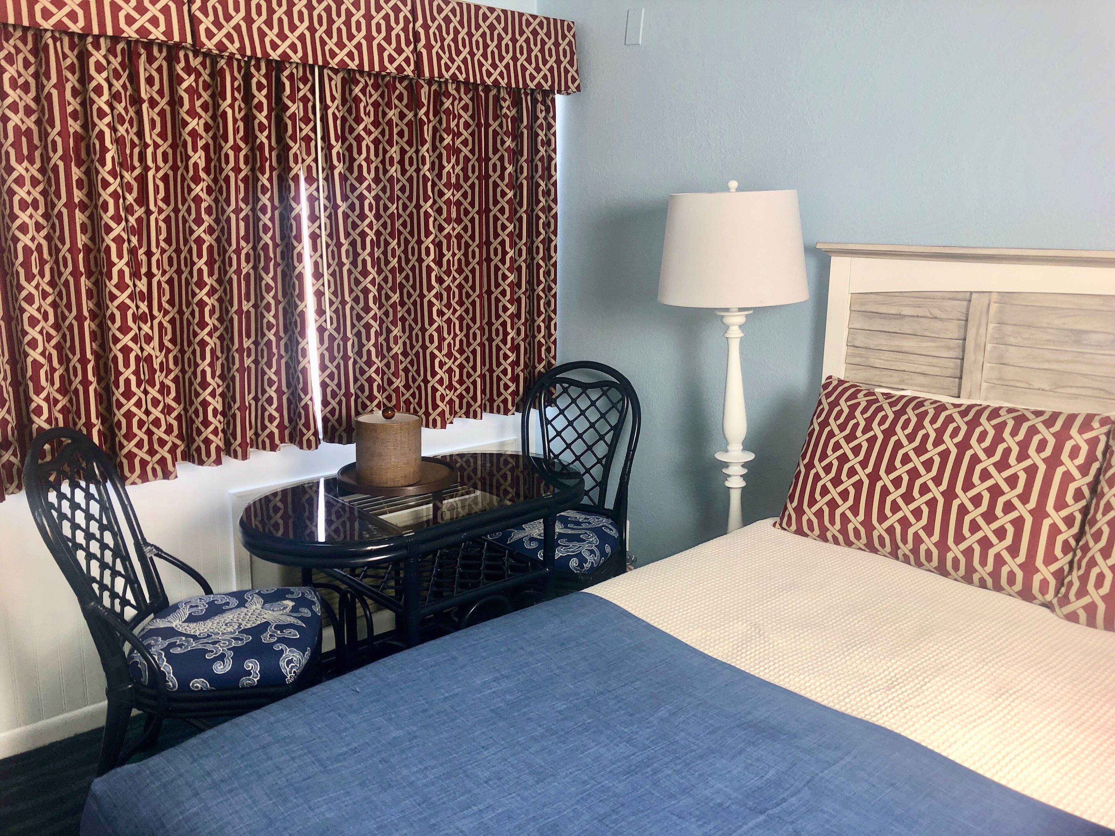 Habitació d'hotel amb un llit, una taula amb cadires, una làmpada i cortines estampades.
