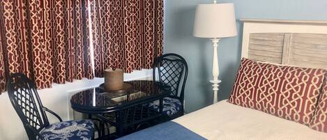 Habitación de hotel con una cama, una mesa con sillas, una lámpara y cortinas estampadas.