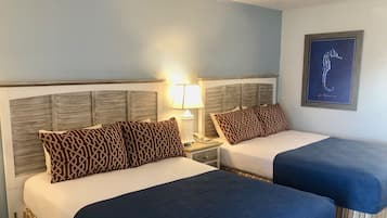 A hotel room with two beds, each with a wooden headboard, a nightstand with a lamp, and a framed seahorse artwork on the wall.