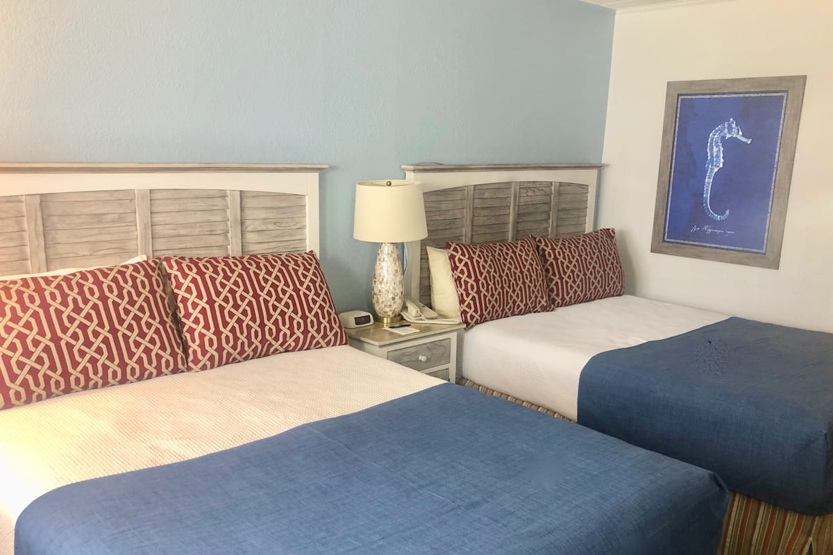 A hotel room with two beds, a nightstand with a lamp, and a framed seahorse artwork on the wall.