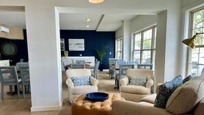 Un salon moderne avec un canapé beige, un pouf rond et un coin repas comprenant des chaises bleues et une table.