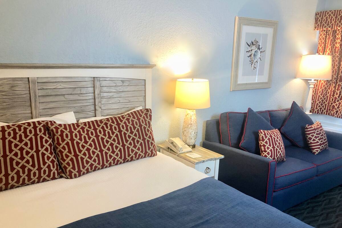 A hotel room with a bed, a sofa, and two lamps.