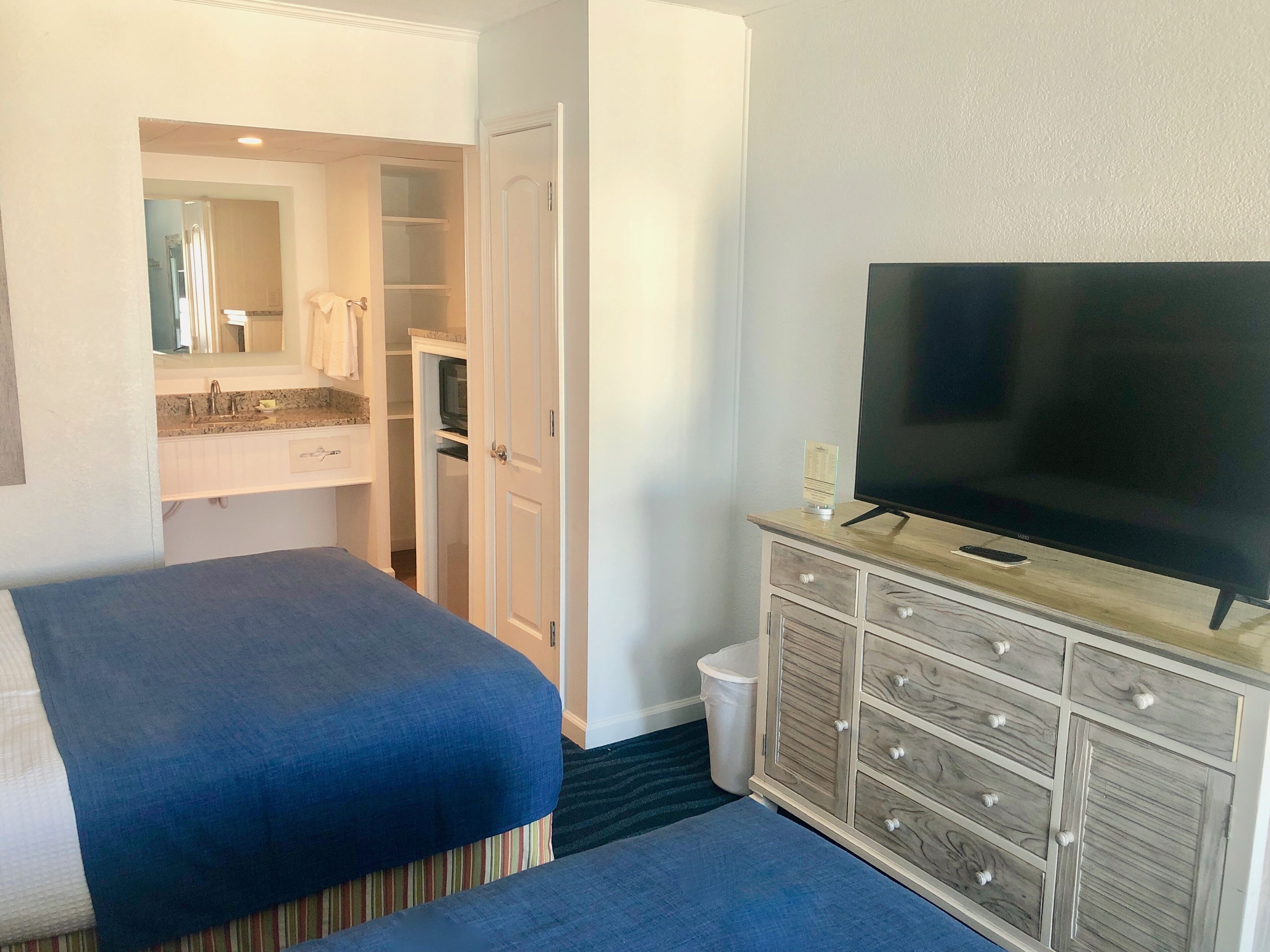 Habitación de hotel con dos camas, televisor, cómoda y baño con lavamanos y espejo.