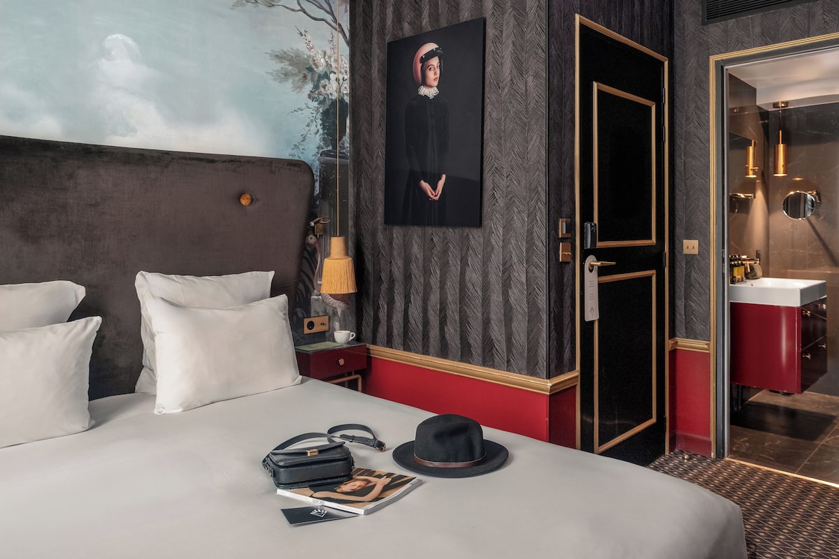 Une chambre d’hôtel avec un grand lit, une table de chevet, un tableau, une porte et une salle de bain visible à travers une porte ouverte.