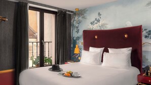 Habitación de hotel con una cama grande, una mesita de noche, una lámpara y vistas al balcón exterior.