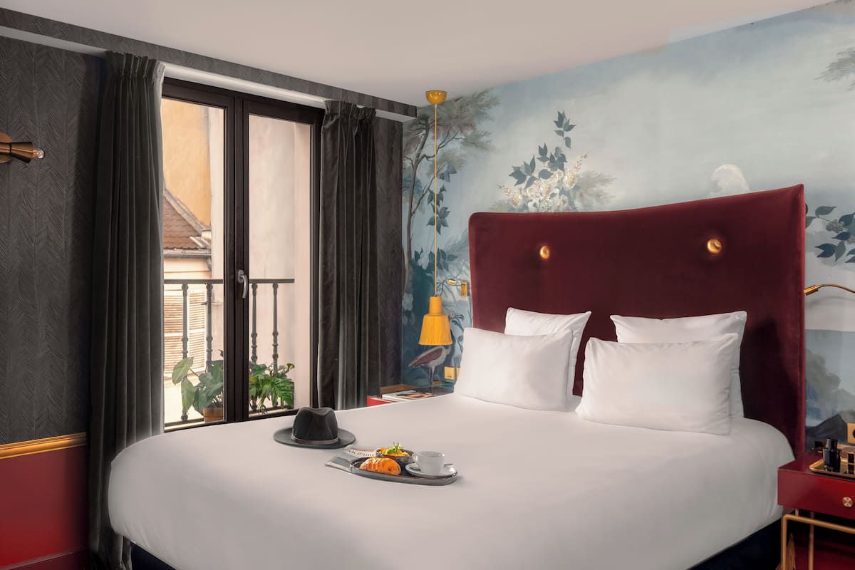 Une chambre d’hôtel avec un grand lit, une table de chevet, une lampe et une vue sur le balcon extérieur.
